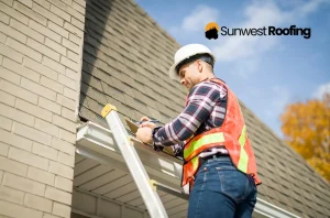 Roofing contractor in a hard hat and safety vest inspecting a house roof.
