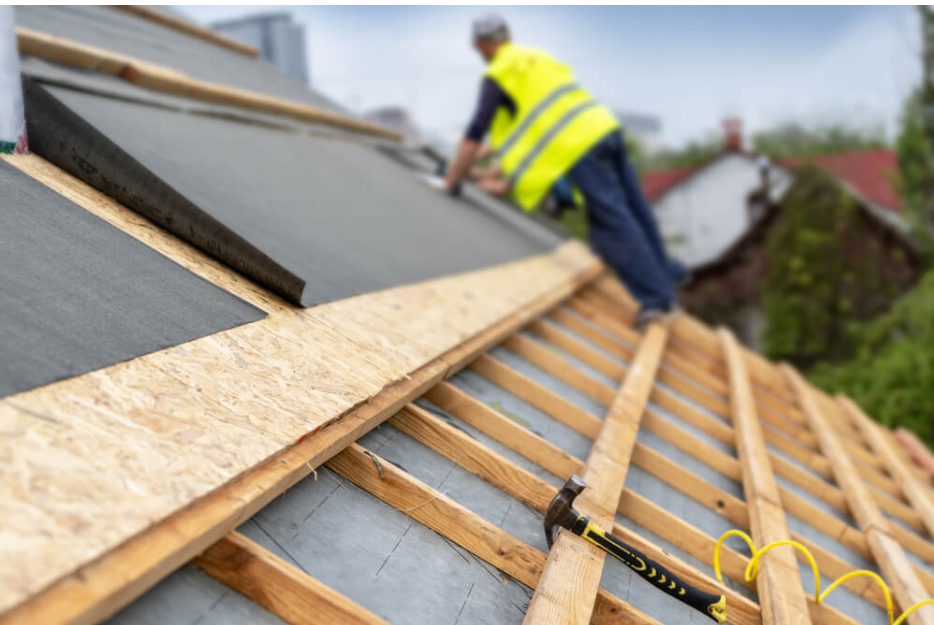 A claw hammer on wooden roof framing with a blurred roofer working in the background.